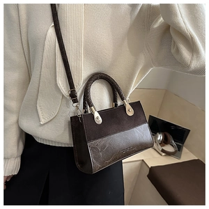 Detail of deep brown textured leather bag with woven handle and gold metal accents