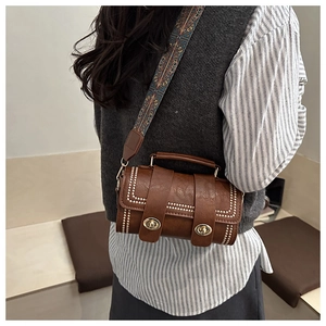 Detail of vintage brown cylinder bag featuring metallic rivet trim and ethnic patterned strap