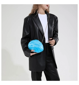 Blue marble acrylic shell clutch with gold chain strap held by a model in black