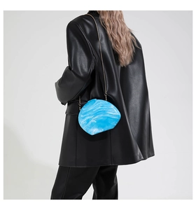 Detail of blue marble acrylic shell clutch with gold chain on model in black leather jacket