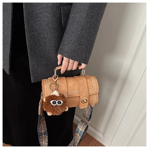 Detail of brown barrel bag with rivet straps, ethnic strap, and plush monster charm