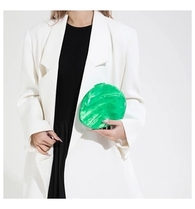 Macro shot of green marbled acrylic dinner clutch bag held by a person in a white suit