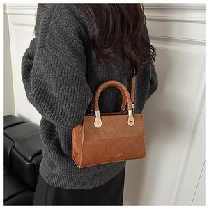 Detail of a brown suede and leather handbag featuring a woven handle and gold hardware