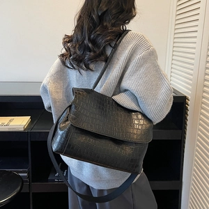 Black crocodile pattern tote bag with wide strap worn by model in minimalist setting
