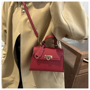 Detail der roten Handtasche mit Litschi-Muster und Goldschloss auf beigem Trenchcoat