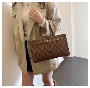 Détail d'un sac cabas tressé marron avec des coins en cuir et une boucle métallique