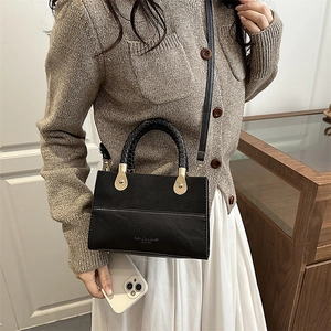 Minimalist black leather crossbody bag featuring woven handles and gold-toned hardware