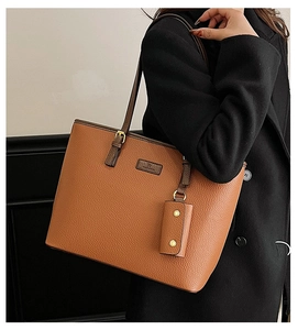 Detail of a brown lychee pattern leather tote bag with a matching charm and metal logo tag