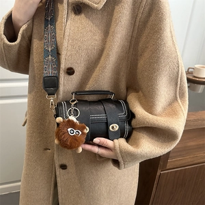 Retro black leather crossbody bag with wide ethnic strap and monster charm on a camel coat