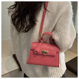 Detailaufnahme einer rosa Handtasche aus Leder mit goldener Schnalle auf weißem Pullover