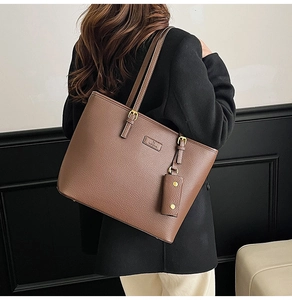Detail of a brown lychee pattern leather tote bag with gold buckles and side pendant