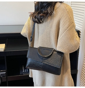 Detail of black textured leather crossbody bag with silver metal handle on a model