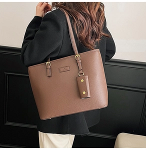 Detail view of brown pebbled leather tote bag with gold metal buckle and logo plaque