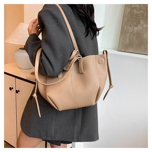 Detailed side view of beige lychee textured tote bag with elegant decorative side laces
