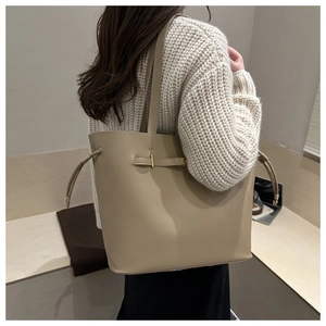 Chic beige faux leather tote bag with gold buckle detail worn by a model in white sweater