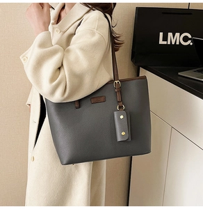 Detail of grey lychee leather tote bag with dark brown straps worn on a beige coat