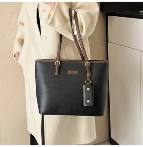 Detail of black pebbled leather tote bag with brown handles and a mini pouch charm