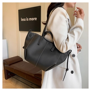 Detail view of black lychee grain leather tote bag with contrast stitching on model