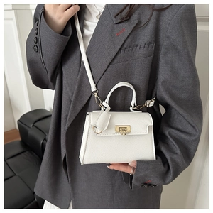 Dettaglio borsa Kelly bianca in pelle martellata con chiusura dorata indossata con blazer