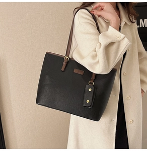 Detail of black pebbled leather tote bag with brown straps worn by a model in a beige coat