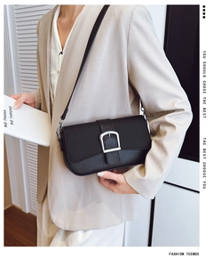 Détail d'un sac à bandoulière en cuir grainé noir avec boucle argentée porté sur un blazer