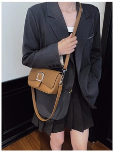 Sac bandoulière marron avec boucle argentée porté par un modèle en blazer gris