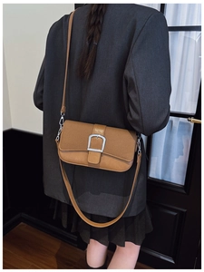 Détail du sac bandoulière en cuir et toile avec boucle argentée sur un blazer gris chic