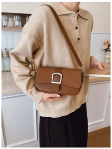 Détail d'un sac d'épaule vintage en cuir marron avec boucle argentée porté par un modèle