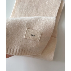 Close-up of beige knitted scarf featuring soft ribbed edges and a minimalist emo fabric label