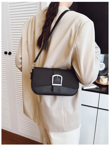 Détail d'un sac bandoulière noir avec boucle argentée porté à l'épaule d'un mannequin