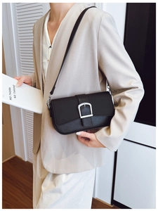 Détail du sac bandoulière noir mat avec boucle argentée porté sur un blazer beige