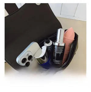 Gros plan sur l'intérieur spacieux de ce sac bandoulière en cuir noir mat avec objets