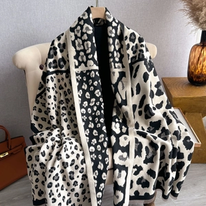 Chic black and white leopard print knitted scarf with fringe, draped on an armchair