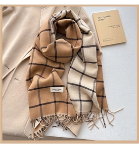 Detail of plaid cashmere-feel scarf with soft fringe edges over a beige wool coat