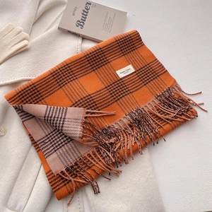 Detail view of orange plaid scarf with fringe on white coat with book and gloves