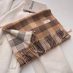 Detail of classic plaid scarf with fringe and tag on elegant white coat background