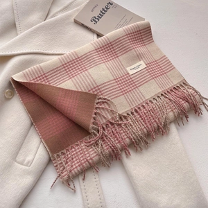 Detail of pink and brown plaid knit scarf with fringes on beige wool coat and book