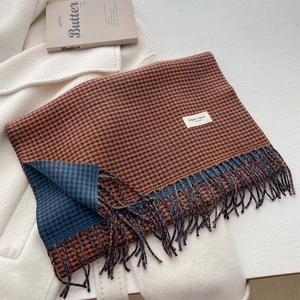 Dettaglio di sciarpa pied de poule arancione con nappe ed etichetta su cappotto bianco