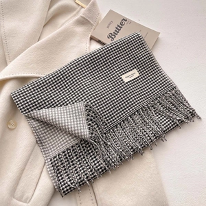 Sciarpa classica pied de poule bianca e nera con nappe ed etichetta su un cappotto beige