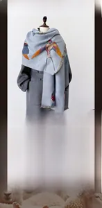 Light blue winter scarf with bird print and soft fringe detail on a grey coat