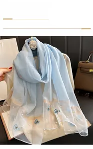 Détail d'une écharpe en soie bleu clair avec broderie papillon et perles élégantes