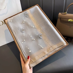 Détail d'une écharpe en soie grise avec bordure dorée, perles et papillons argentés en coffret