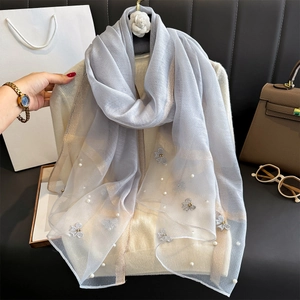Détail d'un foulard en soie bleu clair avec broderie papillon et accents de perles