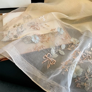 Dettaglio macro di sciarpa in seta champagne con ricami di fiori e fiocchi raffinati