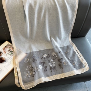 Dettaglio di sciarpa in seta ricamata con fiori e farfalle su superficie di pelle grigia
