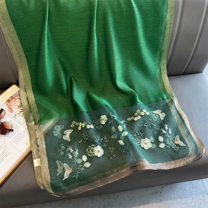 Dettaglio sciarpa di seta verde scuro con ricamo floreale giallo e bordo dorato