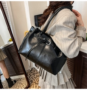 Détail d'un grand sac cabas noir en cuir avec boucle métallique porté par un mannequin