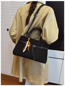 Detail of black faux suede tote bag featuring silver buckle and beaded tassel charm