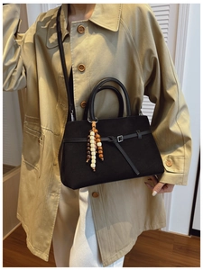 Black matte leather tote bag with wooden bead charm shown on a khaki trench coat