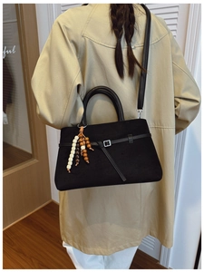 Detail of black suede tote bag with wooden bead charm and shoulder strap on trench coat